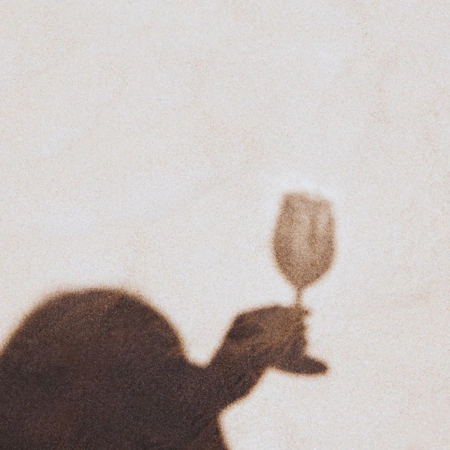 A glass of white wine casting a shadow on sand-coloured linen